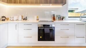 Une cuisine moderne avec des meubles blancs, un four encastré et une hotte de cuisson en acier inoxydable.