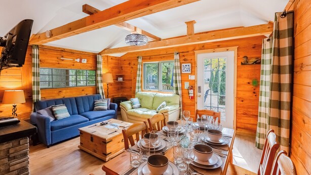 Ein gemütliches Blockhaus-Interieur mit einem Esstisch für vier Personen, einem blauen Sofa und einem grünen Sessel.
