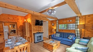 Ein Interieur einer Holzhütte mit Esstisch, blauem Sofa, Couchtisch und Kamin.