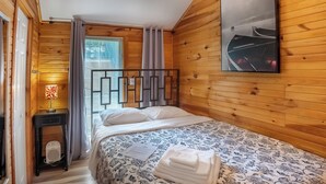 Una habitación con paneles de madera, una cama, una mesita de noche, una lámpara y un ventanal con cortinas.