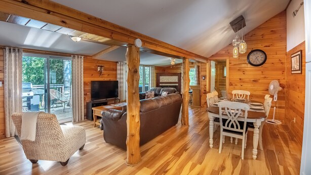 Interior acogedor de una cabaña con piso de madera, un sofá, una mesa de comedor y un televisor.