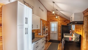 Una cocina compacta con armarios blancos, una estufa negra y paredes de madera.