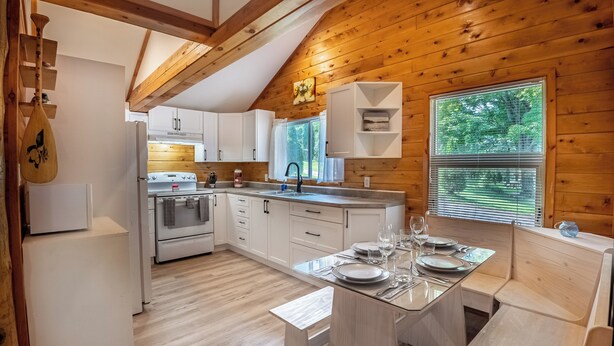 A modern kitchen with white cabinets, a built-in oven, and a dining area with a bench. - Springwood Cottage Resort - Cottage 5 (Arden)