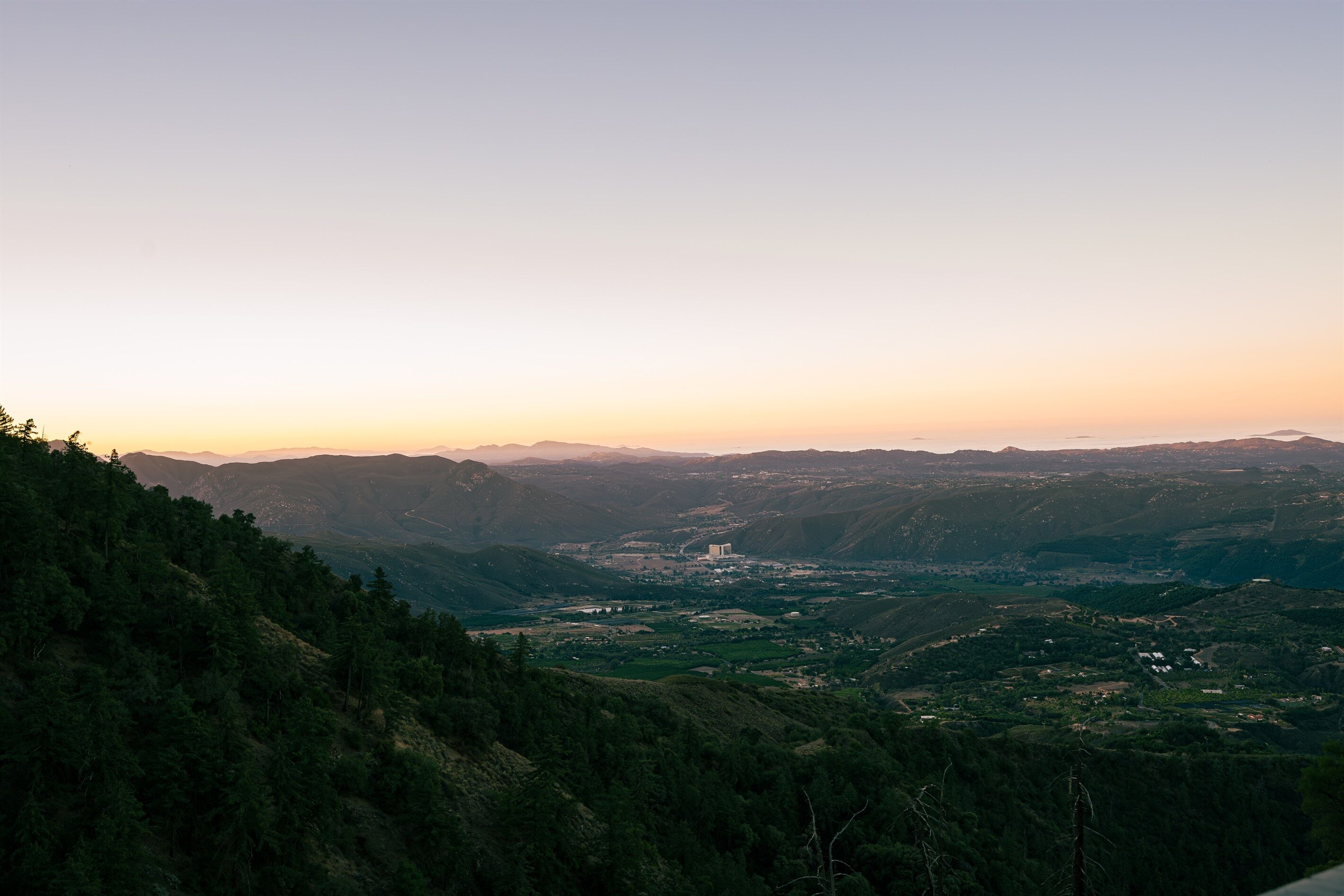 A panoramic view of a mountainous landscape with a valley, a prominent building, and dense forested areas.