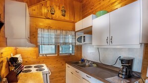A compact kitchen with wooden walls, a stove, white cabinets, a microwave, and a coffee maker. - Springwood Cottage Resort - Cottage 8 (Arden)