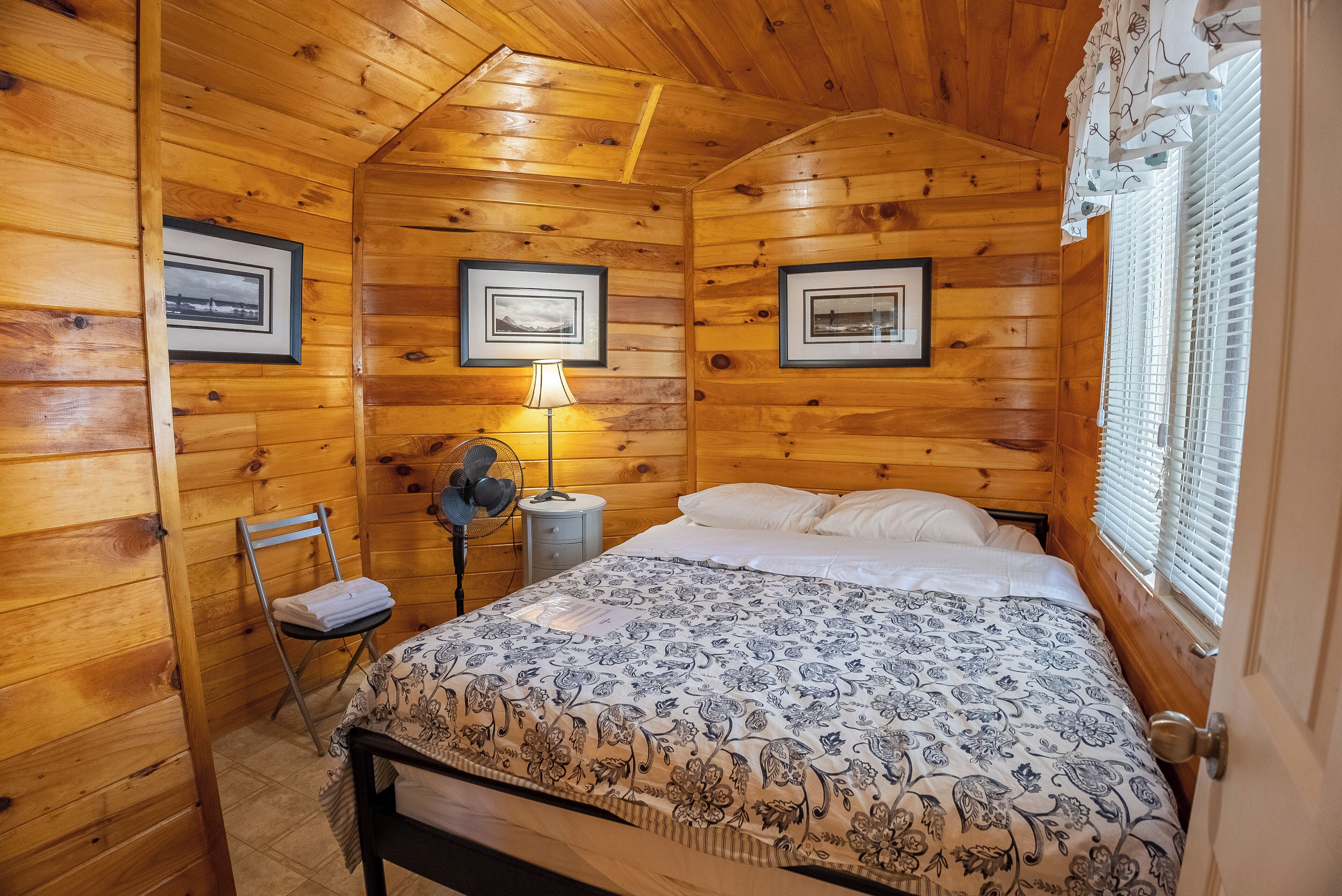 Ein Schlafzimmer einer Holzhütte mit einem Bett, einem Sessel, einer Lampe und gerahmten Bildern an den Wänden.