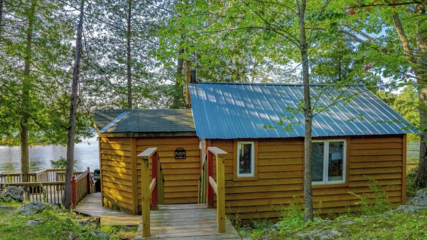 A wooden cabin with a metal roof, a deck, and a small window. - Springwood Cottage Resort - Cottage 8 (Arden)