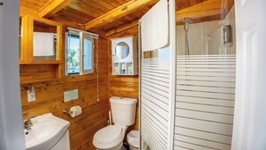 A compact wooden cabin bathroom with a sink, toilet, and shower. - Springwood Cottage Resort - Cottage 8 (Arden)