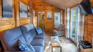 Een gezellig interieur van een chalet met een bank, een gestreept fauteuil, een televisie en kunstwerken aan de muren.