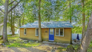 Een klein houten huisje met een blauwe deur, omringd door bomen en een steiger.