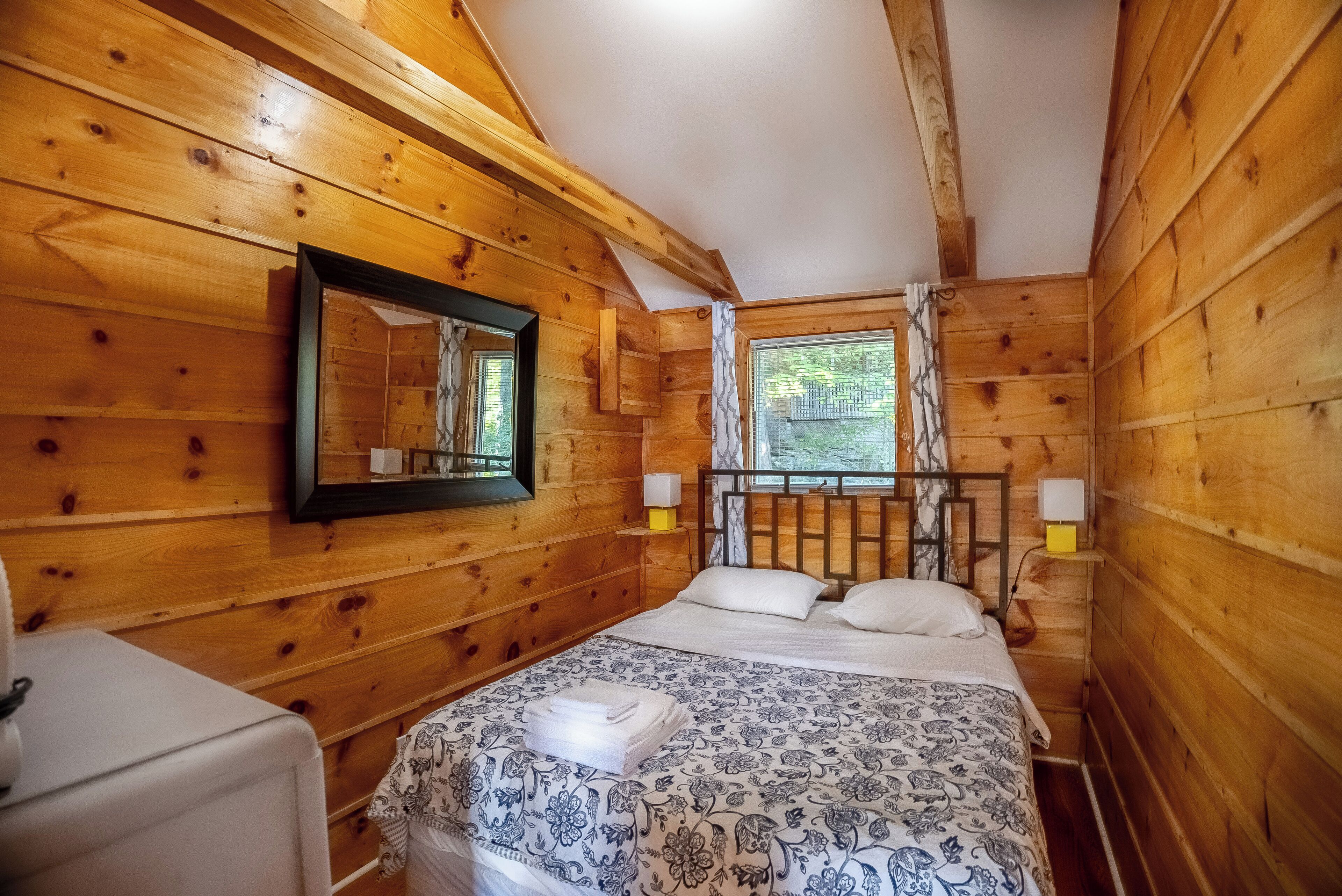 Une chambre dans une cabane en bois, avec un lit, un miroir et une fenêtre.