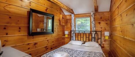 Une chambre dans une cabane en bois, avec un lit, un miroir et une fenêtre.