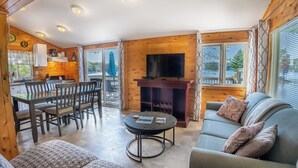 Ein gemütliches Blockhaus-Interieur mit Essbereich, Wohnzimmer mit Sofa und Kamin sowie Küche mit Holzwänden und Fernseher.