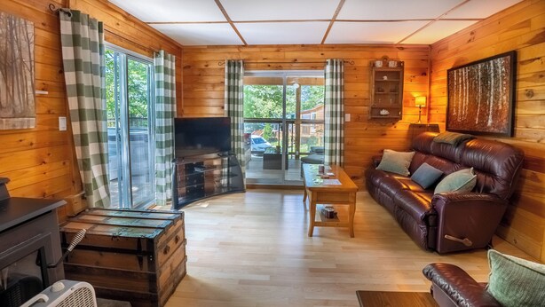 A cozy cabin interior with a wooden interior, a leather sofa, a television, and a fireplace. - Springwood Cottage Resort - Cottage 12 (Arden)