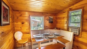 A wooden cabin with a dining table set for four, a bench, and a chair. - Springwood Cottage Resort - Cottage 12 (Arden)