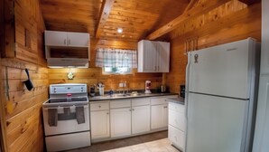 A kitchen with wooden walls, white cabinets, a stove, a sink, and a refrigerator. - Springwood Cottage Resort - Cottage 12 (Arden)