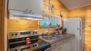 Ett kök med träpanel på väggarna, ett vitt kylskåp, köksmaskiner i rostfritt stål och ett fönster med utsikt över träd.