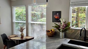 Una cocina moderna con encimera de mármol, un comedor con mesa y sillas, y una ventana con persianas.