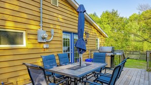 A wooden deck with a table and chairs, a barbecue grill, and a covered umbrella. - Springwood Cottage Resort - Cottage 15 (Arden)