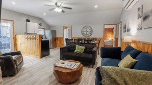 A spacious living area with a high ceiling, wooden flooring, a ceiling fan, and a dining area with a large wall clock. - Springwood Cottage Resort - Cottage 15 (Arden)