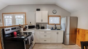 Una cocina con gabinetes blancos, un refrigerador de acero inoxidable, un microondas, una estufa y un lavaplatos.