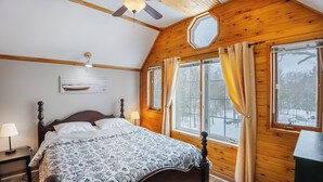 Een slaapkamer met houten lambrisering, een bed, twee bedlampen, een plafondventilator en een raam met gordijnen.