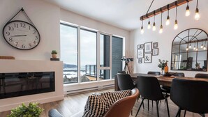 Un salon moderne avec une grande horloge murale, un coin repas avec des chaises et de grandes fenêtres.