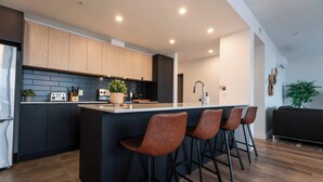 Une cuisine moderne avec des meubles de rangement aux couleurs sombres, un îlot central doté de tabourets de bar et un évier bien visible.