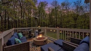 Une terrasse dotée de mobilier d’extérieur, d’un foyer et offrant une vue sur une zone boisée.