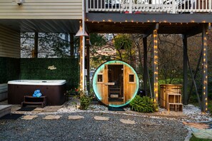 A hot tub and a wooden structure with lights, surrounded by a garden with stepping stones and gravel. - Playhaus Poconos - Sauna, Hottub, Arcade, Karaoke (Tobyhanna)