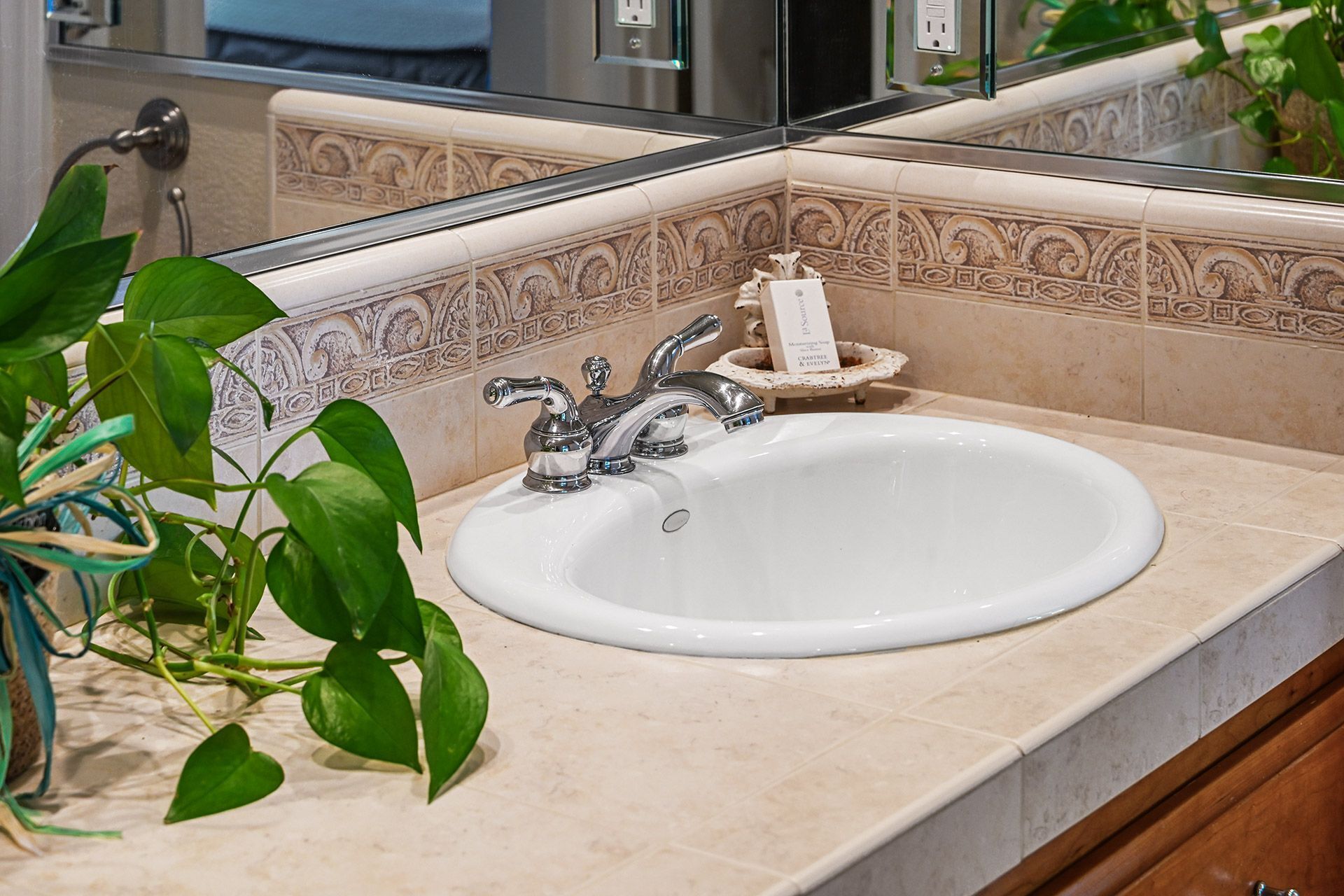 Une salle de bain avec un lavabo blanc, un miroir et un mur recouvert de carreaux décoratifs.