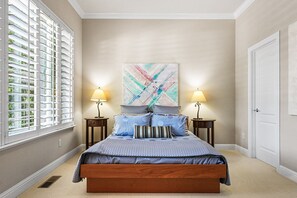 Ein Schlafzimmer mit einem Bett, zwei Nachttischen, einem Fenster mit Jalousien, einer Tür und einem Wandbild im abstrakten Stil.