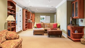 A living room with a sofa, ottoman, and a bookshelf. - The Hideaway | Pool,Tennis Court, Outdoor Kitchen (Santa Rosa)
