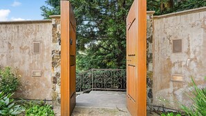 A rustic wooden gate leading to a stone pathway, surrounded by greenery and trees. - The Hideaway | Pool,Tennis Court, Outdoor Kitchen (Santa Rosa)