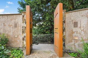 Ein rustikales Holztor, das zu einem steinbelagten Weg führt, umgeben von Grünpflanzen und Bäumen.
