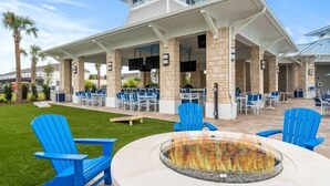 Ein Außenbereich mit einer Terrasse, blauen Adirondack-Stühlen, einer Feuerstelle und einem überdachten Sitzbereich mit Tischen und Stühlen.