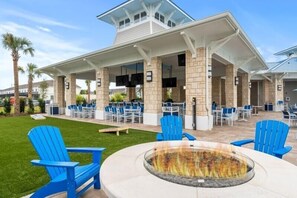An outdoor patio area with blue Adirondack chairs, a fire pit, and a covered seating area with tables and chairs. - 10br Pool Retreat | Theatre • Arcade | Sleeps 24 (davenport)