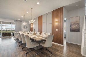 A modern dining area with a long table, white chairs, and a chandelier. - 10br Pool Retreat | Theatre • Arcade | Sleeps 24 (davenport)