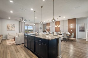 A spacious kitchen with a central island, pendant lighting, and a ceiling fan. - 10br Pool Retreat | Theatre • Arcade | Sleeps 24 (davenport)