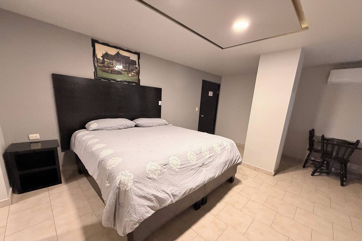 Un dormitorio con cama, mesita de noche, silla y puerta.