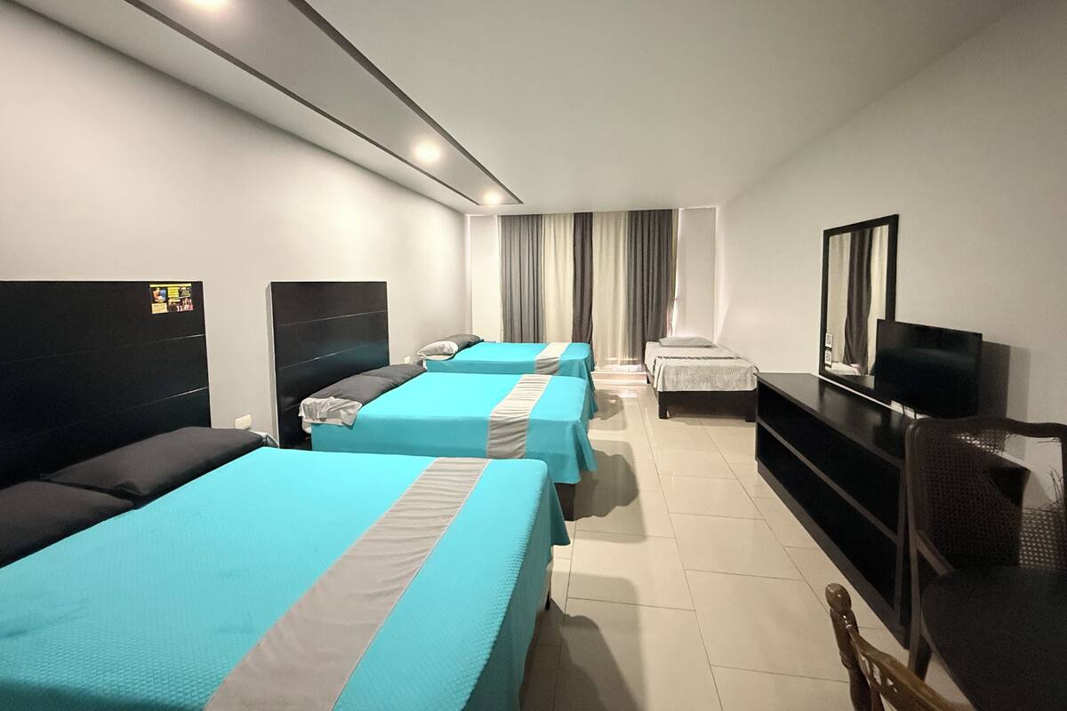 Habitación de hotel con tres camas, televisión, escritorio y una silla.