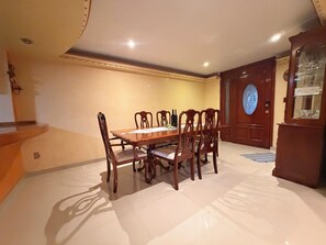 A dining area with a wooden table and chairs, a glass cabinet with dishes, and a door with a circular glass window.