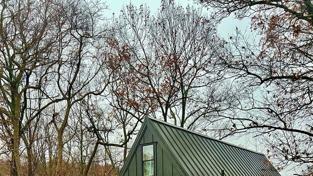 Un pequeño edificio verde oscuro con techo inclinado y terraza de madera.