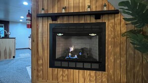 Una pared revestida de madera con chimenea, un extintor y un pequeño estante con adornos.