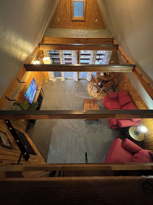 Une pièce de style loft avec un plafond en bois, une télévision, une table à manger avec des chaises et un canapé rouge.