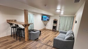 Un salón amplio con una mesa de comedor de madera, dos sillones grises, un sofá gris y un televisor de pantalla plana montado en la pared.