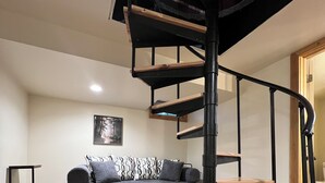 Un interior moderno con una escalera espiral, un sofá oscuro y un suelo de madera.