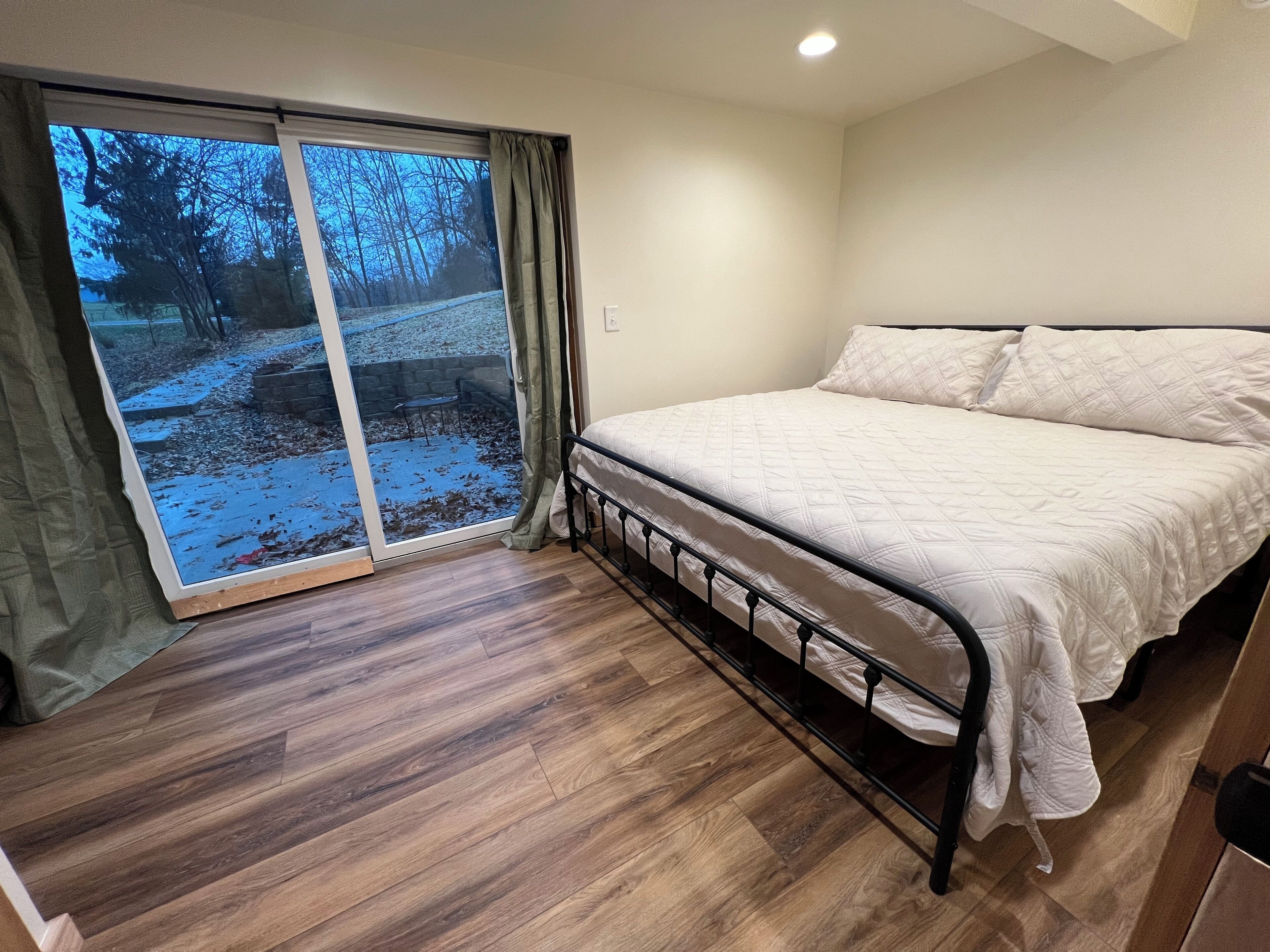 A bedroom with a bed, a sliding glass door leading to a snowy outdoor area, and a wooden floor.