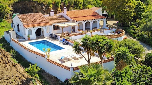Eine Villa mit Swimmingpool, Sitzgelegenheiten im Freien und einem Garten.