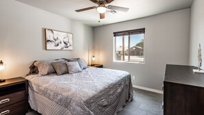 Ein Schlafzimmer mit einem Bett, einem Deckenventilator, einem Fenster und einem Nachttisch.